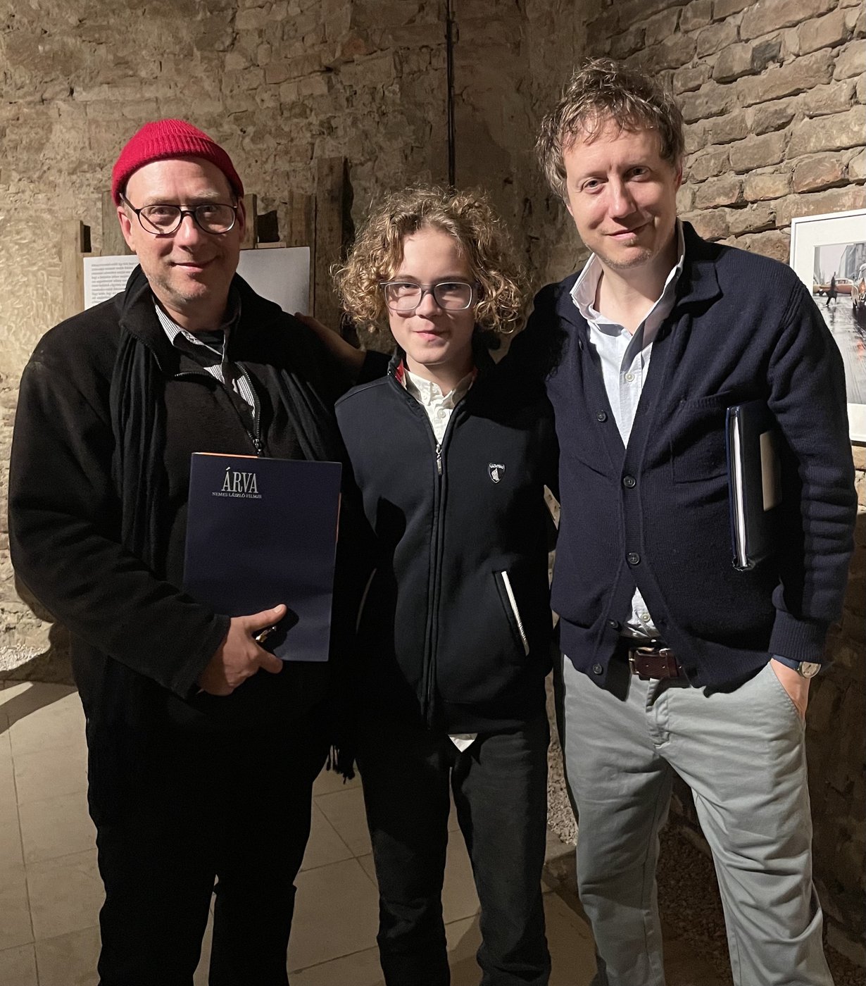 Grego with László Nemes and a young actor holding the Árva press folder, in a vaulted brick room