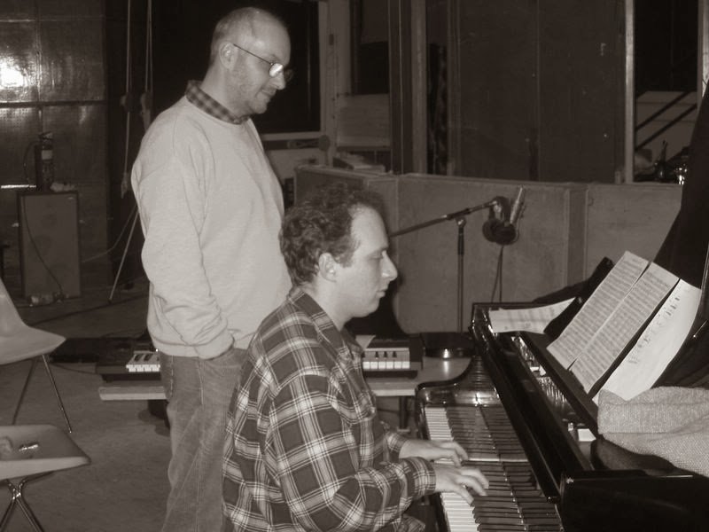 Grego at the grand piano in a studio with Attila László standing behind him, a microphone above the strings