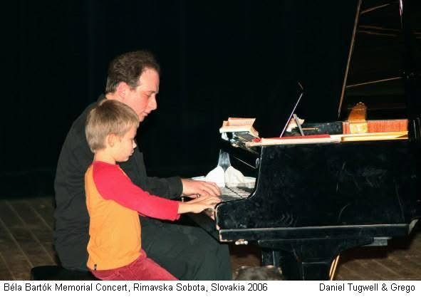 Grego at the grand piano with a small boy playing beside him on stage