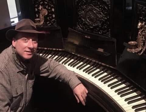 Grego leaning on the curved keyboard of an ornate historic instrument