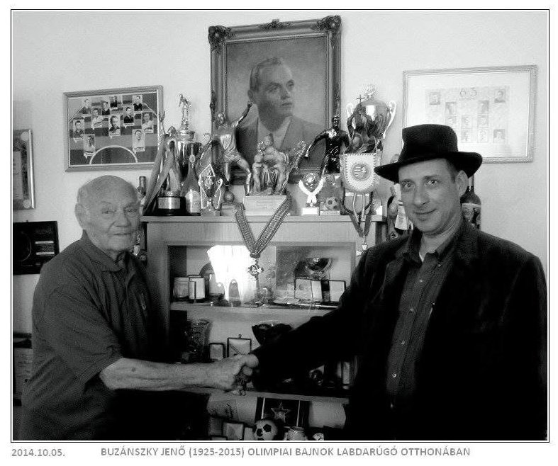 Grego shaking hands with Jenő Buzánszky in a room full of trophies and team photographs