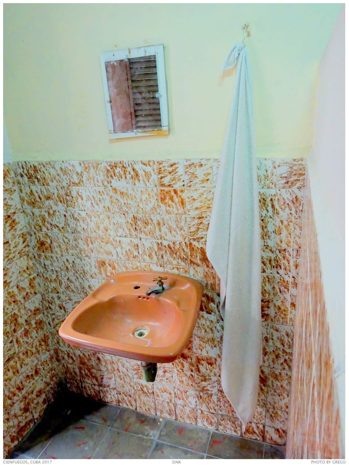 A pink sink and hanging towel against mottled orange tiles