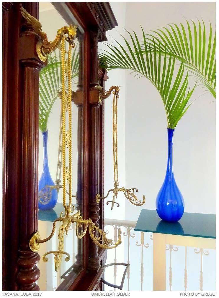 A gilt umbrella holder on a mahogany mirror, a blue vase and palm frond reflected
