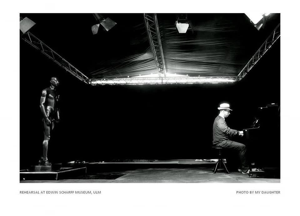 Grego at the piano facing a sculpture during rehearsal in Ulm