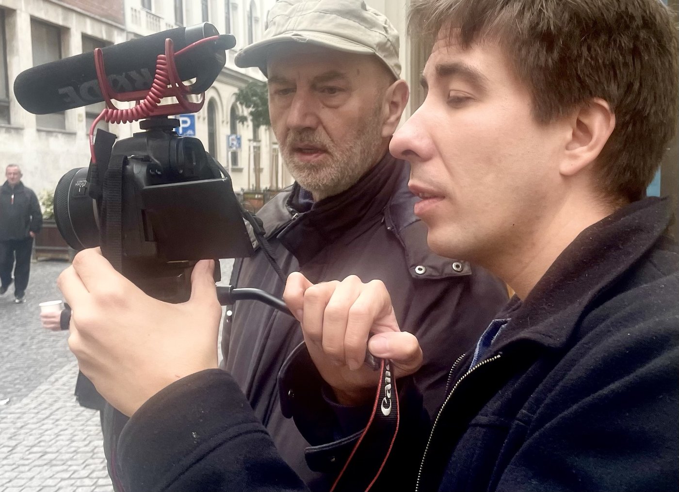 A young cameraman filming in the street with a director watching over his shoulder