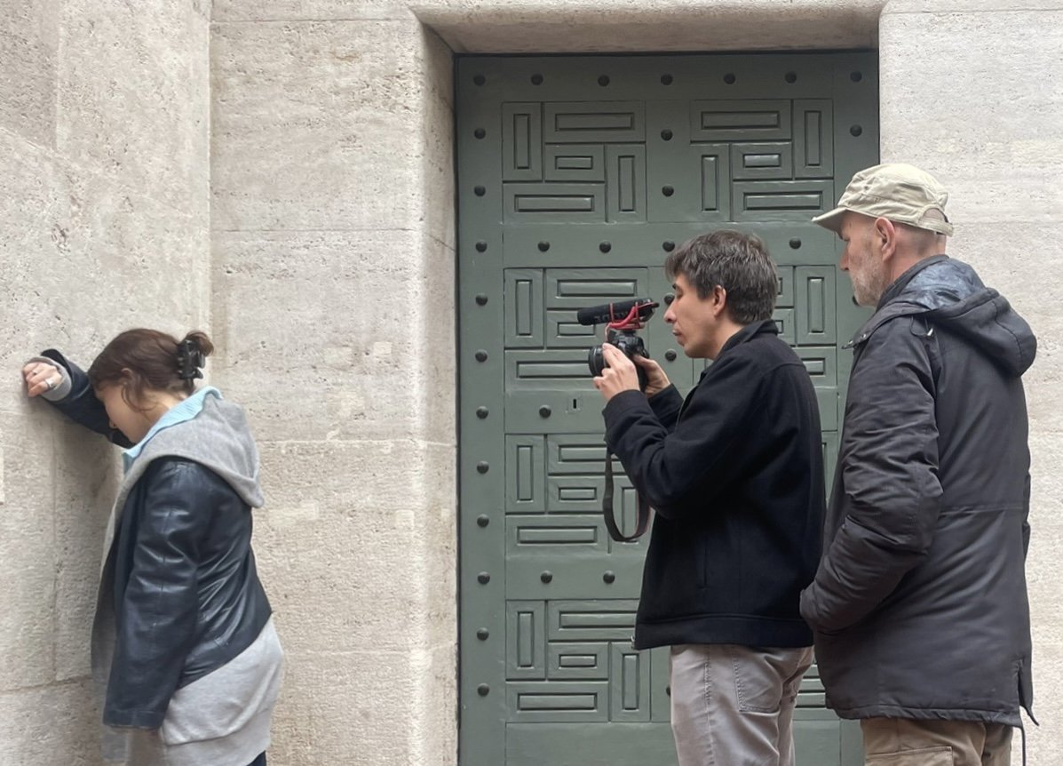 Three people filming beside a heavy green door in a stone doorway