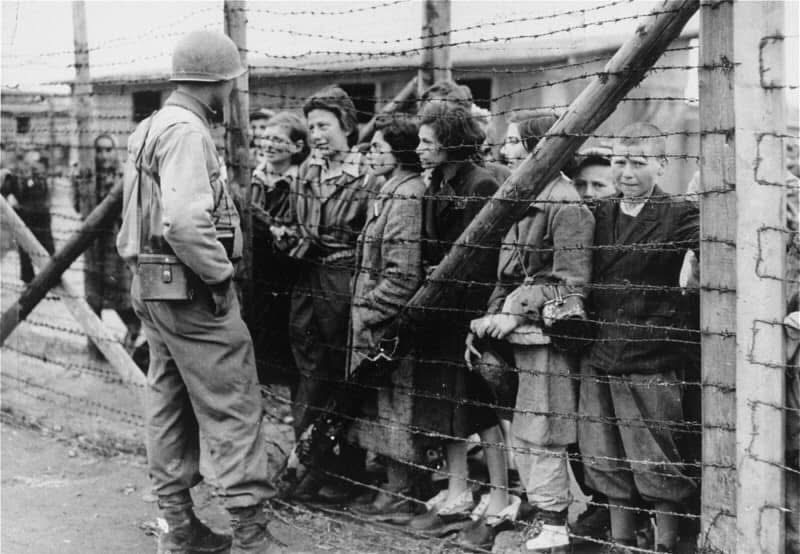 An American soldier facing survivors behind the wire at liberation, May 1945