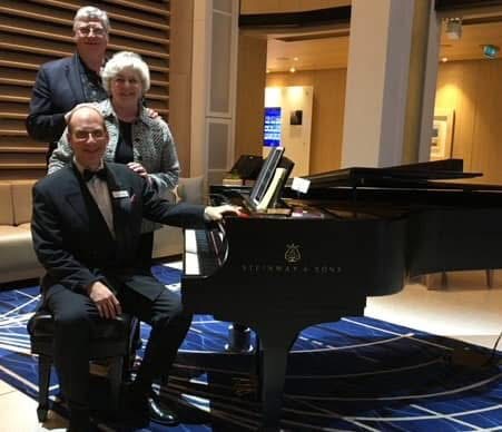 Grego at the Steinway in the ship's atrium with the couple standing behind him