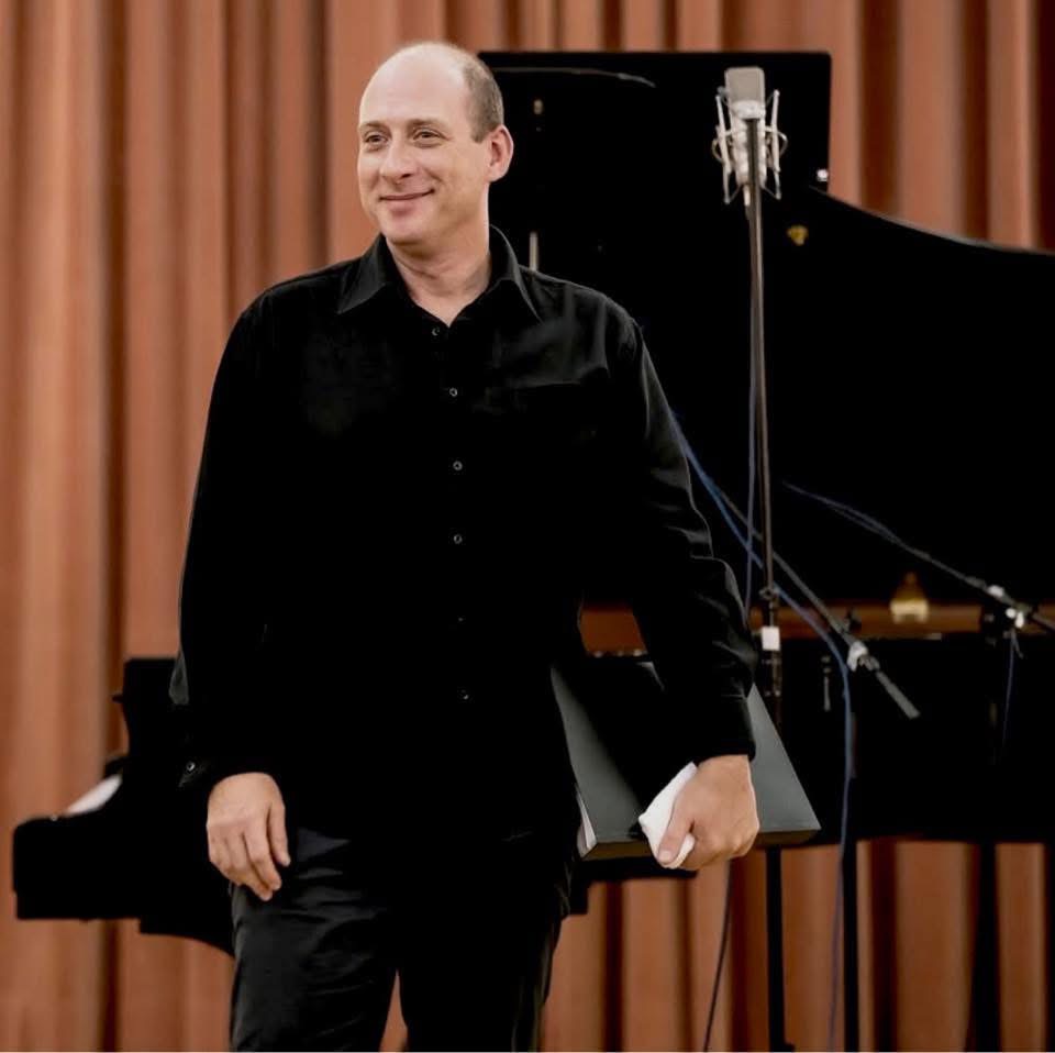 Grego standing beside the piano, score under his arm