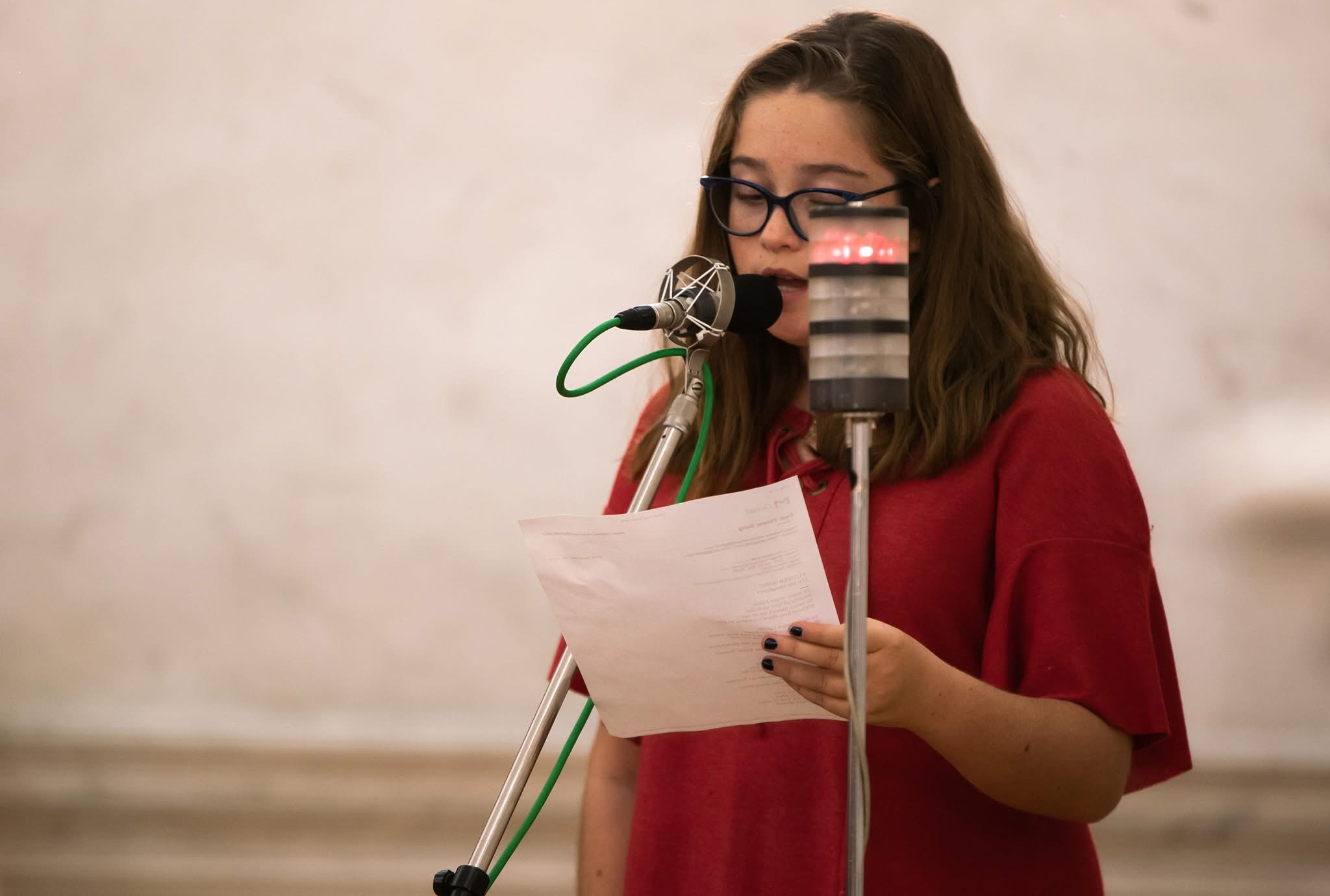 A young woman in red reading from a sheet of paper at two microphones