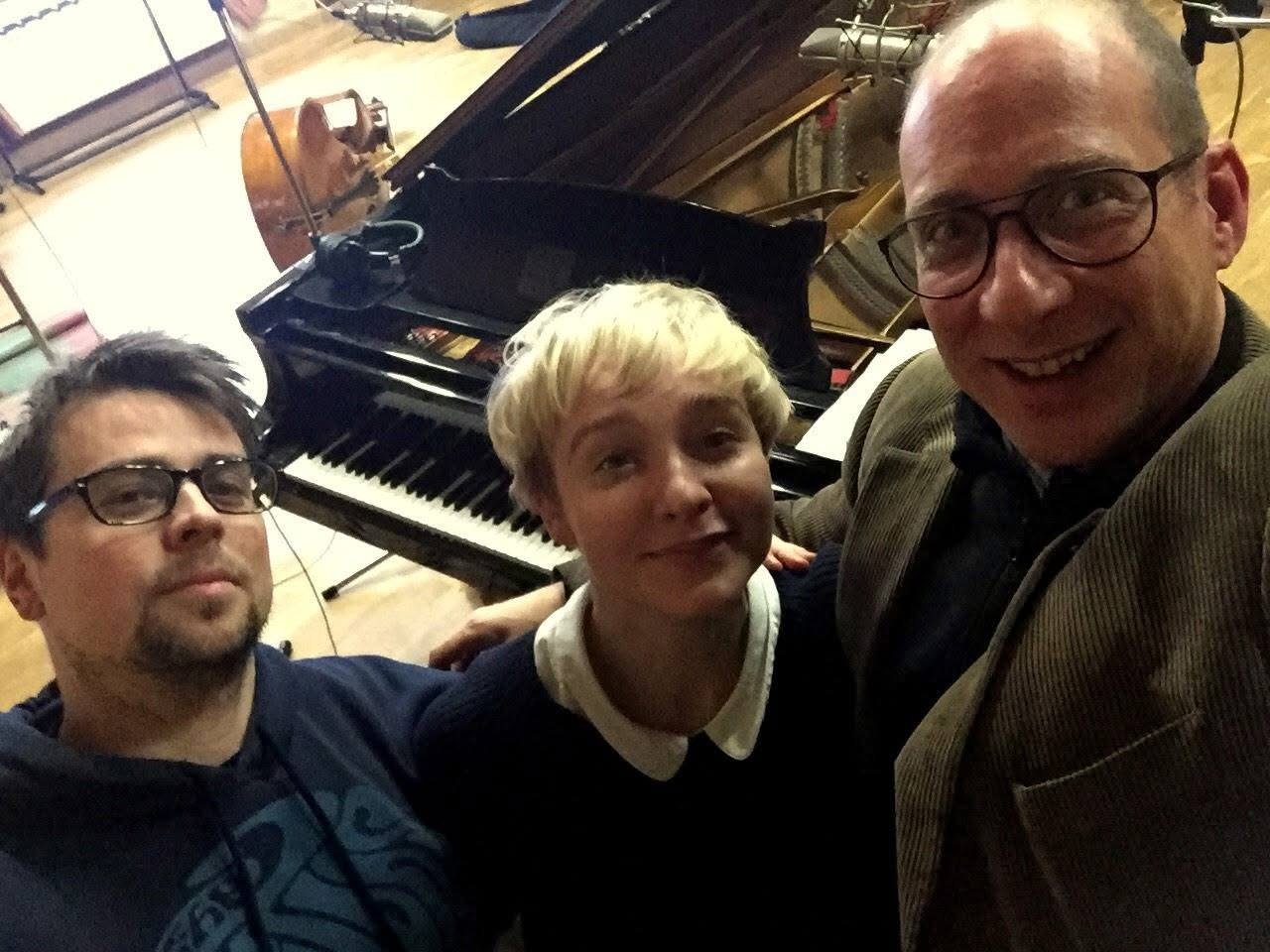 Three people in a recording studio beside a grand piano and a double bass