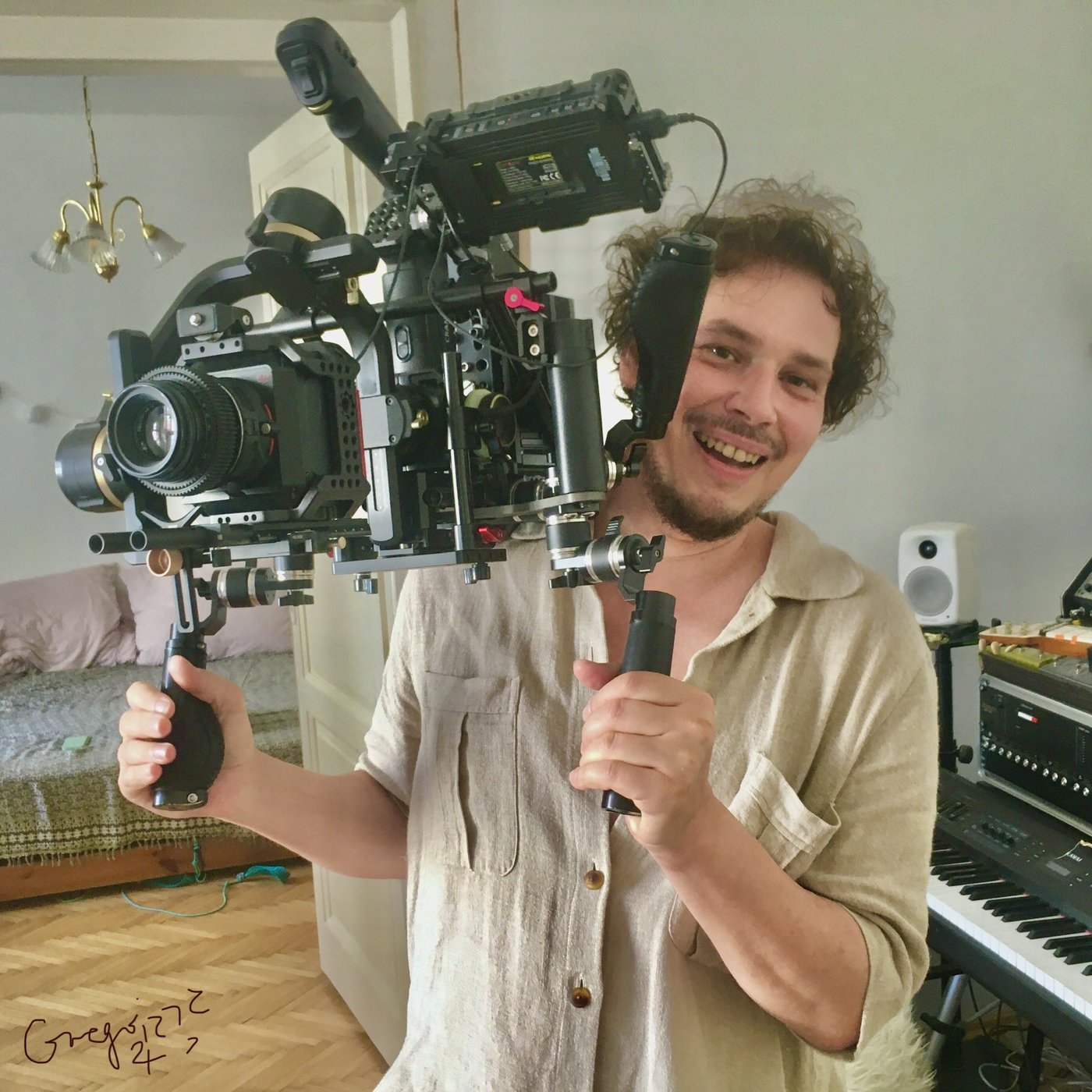 A young film maker grinning behind a camera rig on a gimbal, a keyboard beside him