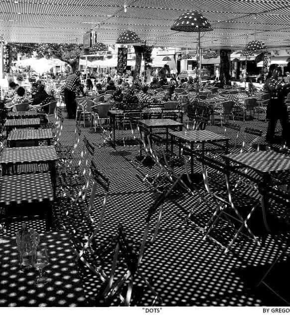Empty café terrace under polka-dot parasols casting dotted shadows