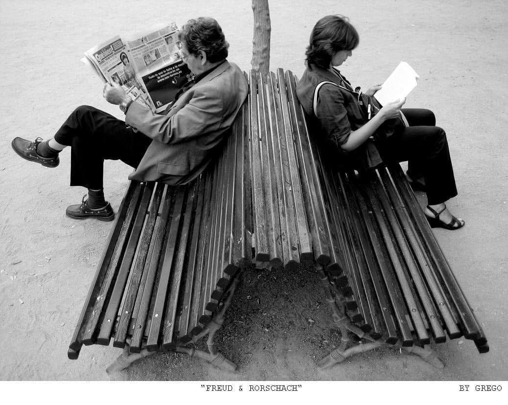 Two people reading back to back on a double bench, forming a symmetrical shape