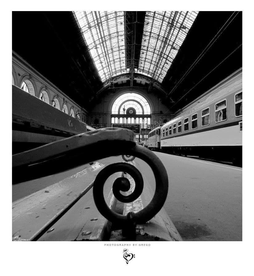 Iron scroll of a station bench with the glass roof of Keleti station behind