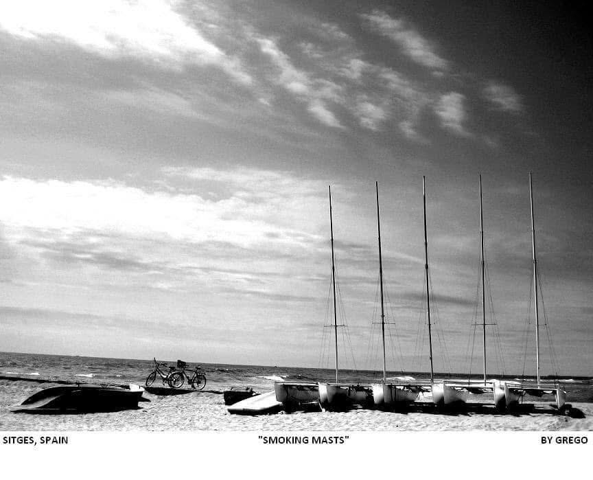 Catamaran masts on a beach against a streaked sky
