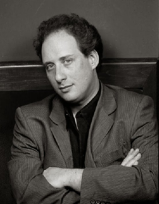 Black and white studio portrait of Grego in a jacket with his arms folded