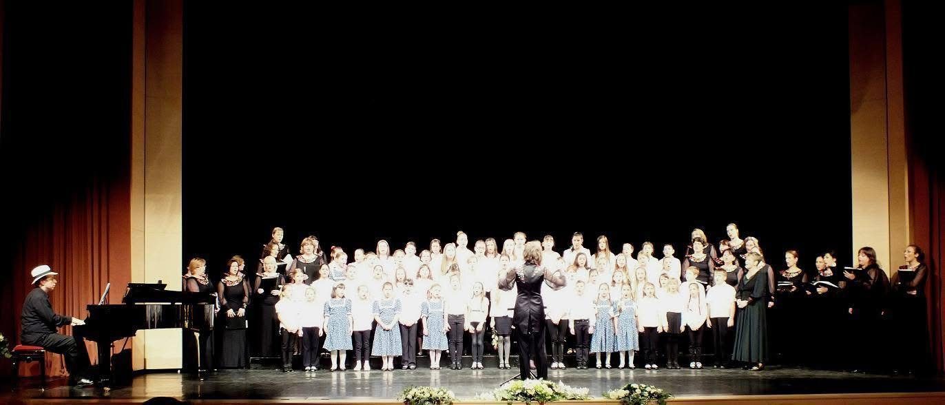 Children's choirs on stage with a conductor and Grego at the piano at the side