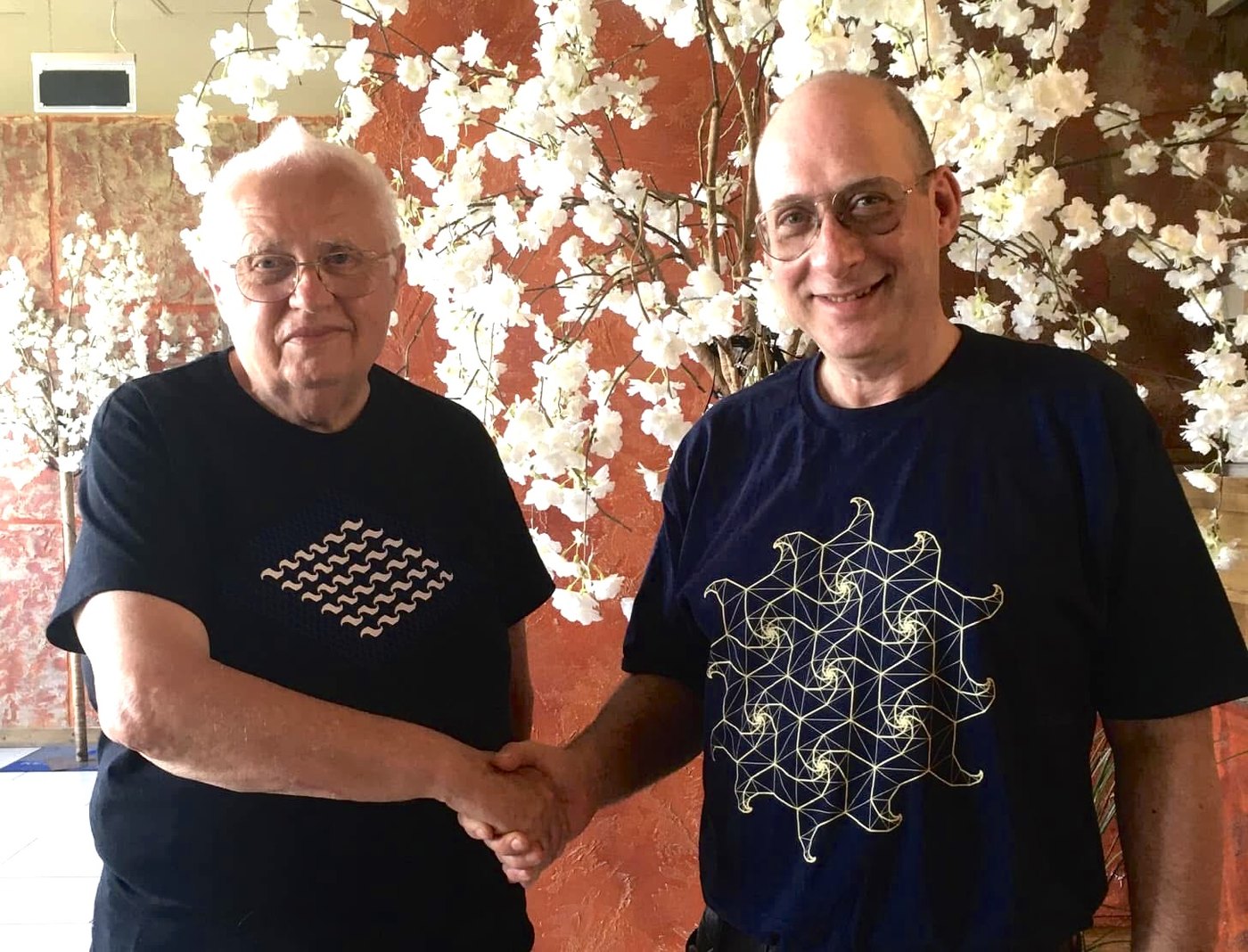 Grego shaking hands with Professor Lajos Szilassi in front of a wall of white blossom