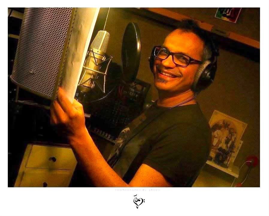 Péter Szolnoki smiling in the studio, headphones on, beside a microphone and pop shield