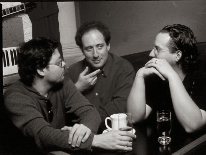 Grego talking with Péter Papesch and Gergő Borlai at a table, a painted keyboard on the wall behind