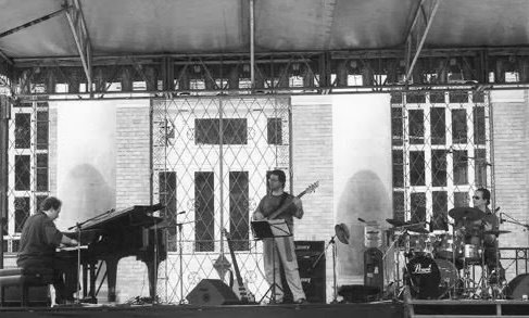 The trio on an open-air bandstand stage, piano at the left, bass in the centre and drums at the right