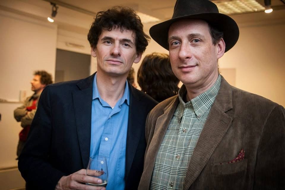 Grego in a dark hat beside the artist Tamás Vészi at a gallery opening