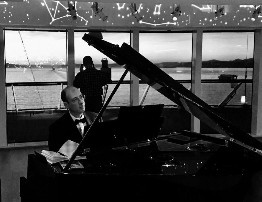 Grego at the grand piano with the fjord through the windows behind him