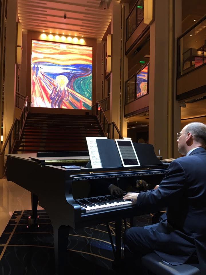Grego playing a grand piano in the atrium beneath a large reproduction of Munch's The Scream