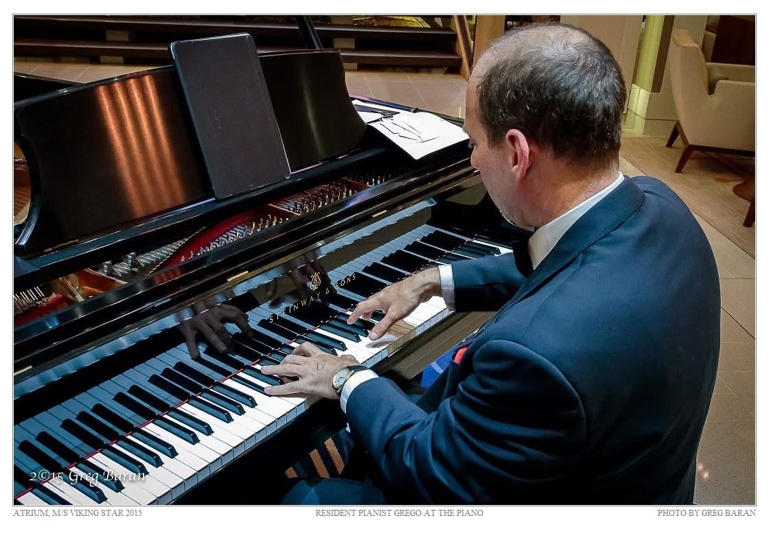 Grego playing a Steinway grand in a ship atrium, seen from behind over his shoulder